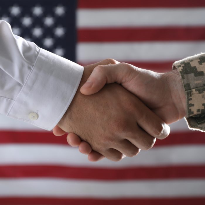 Soldier and businessman shaking hands against flag of USA, closeup