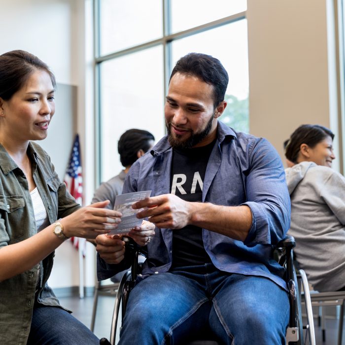 A mid adult woman shares an informational handout for veterans with an army vet in a wheelchair.