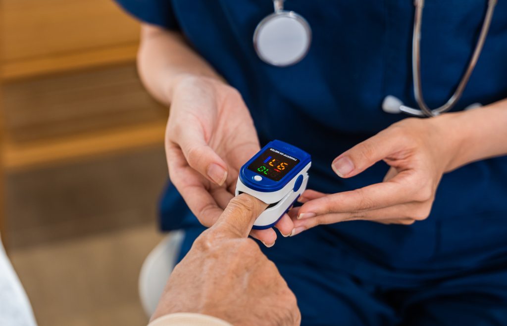 Young woman putting digital oximeter of finger middle aged adult patient for measurement, nurse checking with fingertip pulse oximeter oxygen meter blood monitor finger of senior old man at hospital