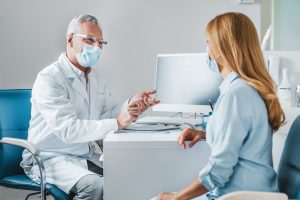 Senior male doctor wear protection face mask talking with patient in clinic office