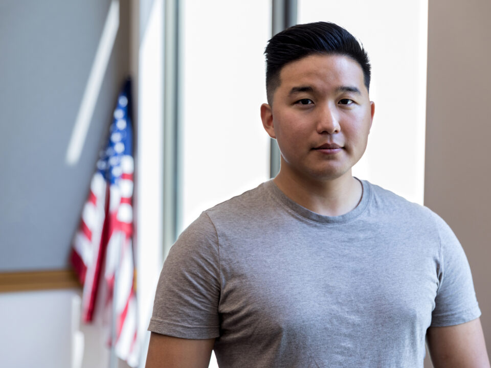 A serious mid adult male veteran poses for a portrait with the American flag in the background.